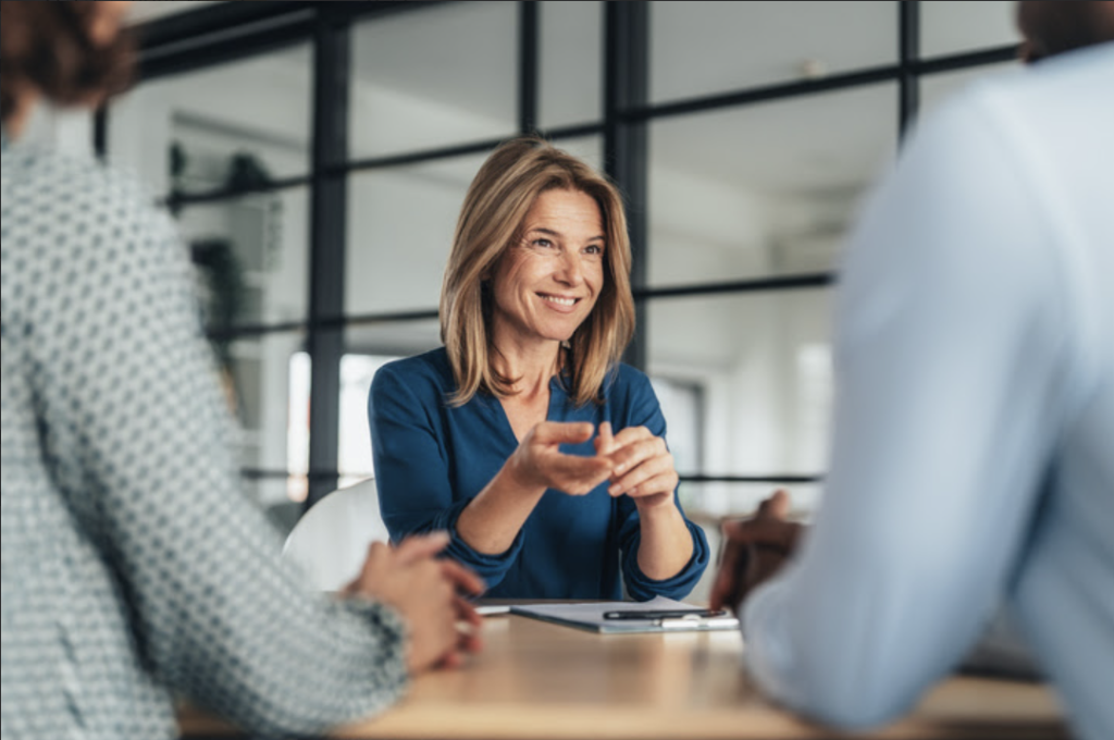 Woman meeting with two people across a desk, with documents in front of her.